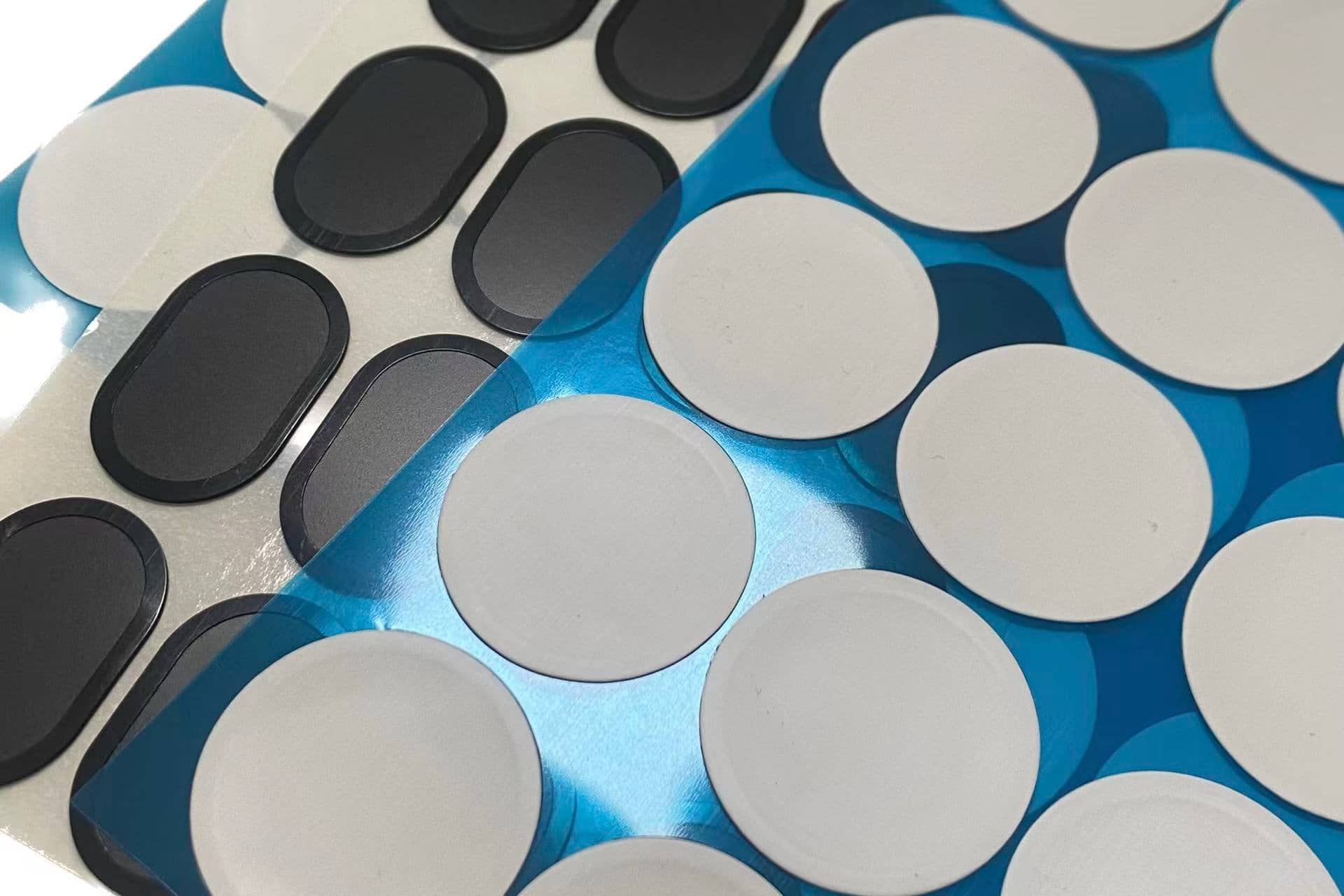 Close-up of die-cut ePTFE membrane samples in white and black, still on blue protective backing